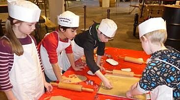 Vier Kinder mit Schürzen und Kochmützen backen Plätzchen